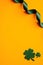 Happy St Patricks Day vertical banner design. Shamrock leaves and green ribbon on orange background. Flat lay, top view, copy