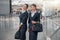 Happy stewardesses with hand luggage standing in airport hall