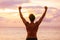 Happy strong man with arms up in success. Silhouette of fit male athlete winner from behind standing at ocean beach