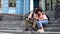 Happy student couple hugging, sitting on university building stairs, youth love