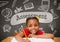 Happy student girl at table against grey blackboard with assessment text and education and school gr