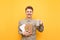 Happy student in shirt and glasses stands on yellow background with cup of hot drink in hand and exercise books, pen and books,