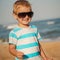 Happy stylish boy in sunglasses and striped t-shirt enjoying life on summer beach