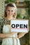 Happy stylish business owner woman in apron showing open sign