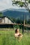 Happy stylish hipster girl sitting and smiling on background of old cottage mountains in summer