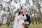 Happy stylish newlywed pair posing in conifer forest with young pine trees. Half-length portrait