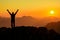 Happy success winning man arms up on mountain at sunset