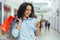 Happy and successful woman shopping for clothes in a supermarket store, Hispanic woman holding a smartphone reading