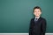 Happy successfull school boy in black suit portrait on green chalkboard background, education concept