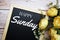 Happy Sunday text on blackboard decorated with flower bouquet on wooden background