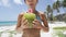 Happy suntan bikini girl drinking fresh coconut water on tropical beach vacation