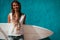 Happy surfer girl with surfboard in front of blue wall