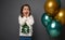 Happy surprised baby girl in sweater with shiny Christmas tree, rejoicing standing near inflated golden and green metallic air