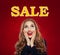 Happy surprised girl looking at sale text on red banner background. Beautiful woman with red lips makeup and long curly hairstyle