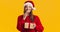 Happy surprised lady in Santa hat holding Christmas gift and laughing, enjoying her present, orange background