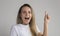 Happy surprised shocked exhilarated young woman with raised index finger coming up with idea. Woman isolated over gray background