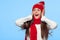 Happy surprised woman looking sideways in excitement. Christmas girl wearing knitted warm hat and mittens, isolated on blue backgr