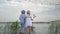 Happy sweet children boy and girl with toy windmills walk by hand on wooden bridge on river between green reeds