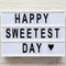 `Happy Sweetest Day` word on modern board over white wooden background, top view. From above, flat lay, overhead