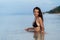 Happy tanned girl in swimsuit sits in ocean and poses on beach at vacation