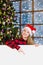 Happy teen girl in christmas hat peeking above white banner and pointing down. Space for text