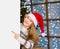 Happy teen girl in red christmas hat peeking above white banner and pointing away