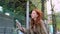 Happy teen girl red hair sitting on big city urban street using smartphone.