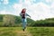 A happy teen girl is skipping across the field. Mountains and sky are in the background. The concept of freedom and