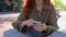 Happy teen redhead girl sitting on big city urban street using smartphone.