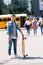 happy teen schoolboy with skateboard standing in front of school bus and group of classmates walking blurred