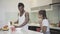 Happy teenage girl clapping as father pouring cereals into bowls in kitchen. Portrait of cheerful African American man