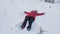 Happy teenage girl making snow angel in winter forest