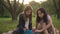 Happy teenage relaxed girls talking sitting on picnic in park at sunset outdoors. Wide shot portrait of carefree