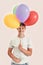 Happy teenaged disabled boy with Down syndrome smiling at camera, holding a bunch of colorful balloons while standing