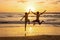 Happy teenager boys, running and playing on the beach on sunset, splashing water and jumping on the sand