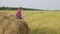 Happy teenager girl on hay stack at farming field. Smiling girl showing thumbs up on countryside field. Hay straw on