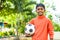 Happy teenager kid holding football by looking camera at garden with copy space - concept of childhood lifestyle, future