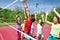 Happy teens with arms up play volleyball near net