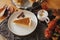 Happy Thanksgiving. Pumpkin pie slice on modern plate and hot coffee on rustic table with linen napkin, autumn flowers and leaves