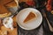 Happy Thanksgiving. Pumpkin pie slice on modern plate and hot coffee on rustic table with linen napkin, autumn flowers and leaves