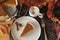 Happy Thanksgiving. Pumpkin pie slice on modern plate and hot coffee on rustic table with linen napkin, autumn flowers and leaves