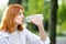 Happy thirsty redhead woman drinking fresh bottled water in summer outdoors