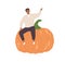 Happy tiny person sitting on huge fresh pumpkin. Smiling man with big autumn vegetable. Farmer and his organic harvest