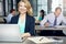 Happy to be working here. Portrait of a businesswoman using a laptop at her desk with her colleagues in the background.