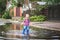 Happy toddler boy running through puddles in rubber boots. Child splashes after rain outside..