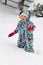 Happy toddler girl in warm coat and knitted hat tossing up snow and having a fun in the winter outside, outdoor portrait