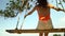 Happy tourist asian woman playing swing under big tree and looking nice view at beautiful beach with slow motion. Asian woman wear