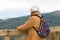 Happy tourist senior woman with backpack standing on observation deck and looking at beautiful mountains covered snow