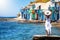Happy tourist woman in white dress enjoys the view to the fishing village of Klima, Milos, Greece