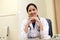 Happy traditional female doctor at her desk in hospital interior